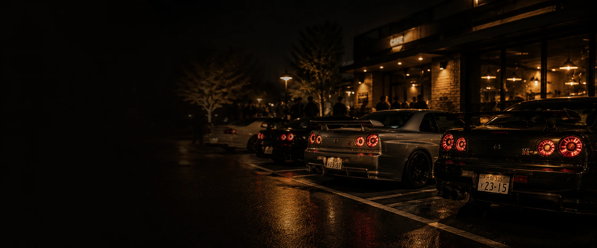A row of Nissan Skyline GT-Rs parked outside a cafe at night.