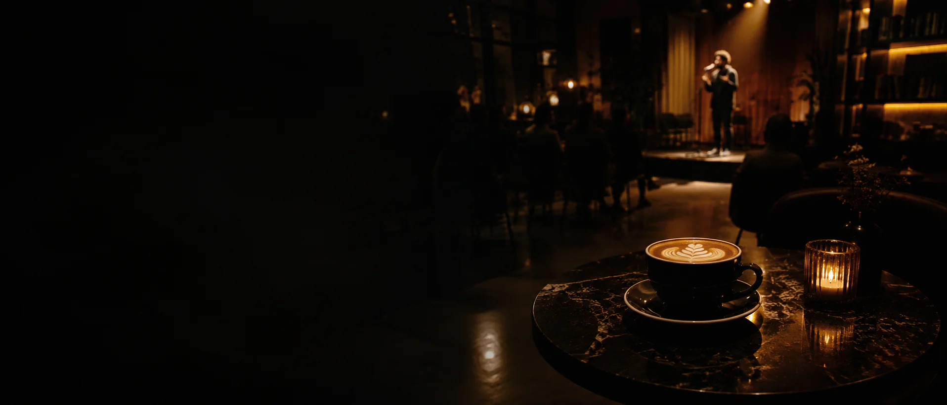 A performer on stage in a dark venue, a coffee on a table in the foreground.